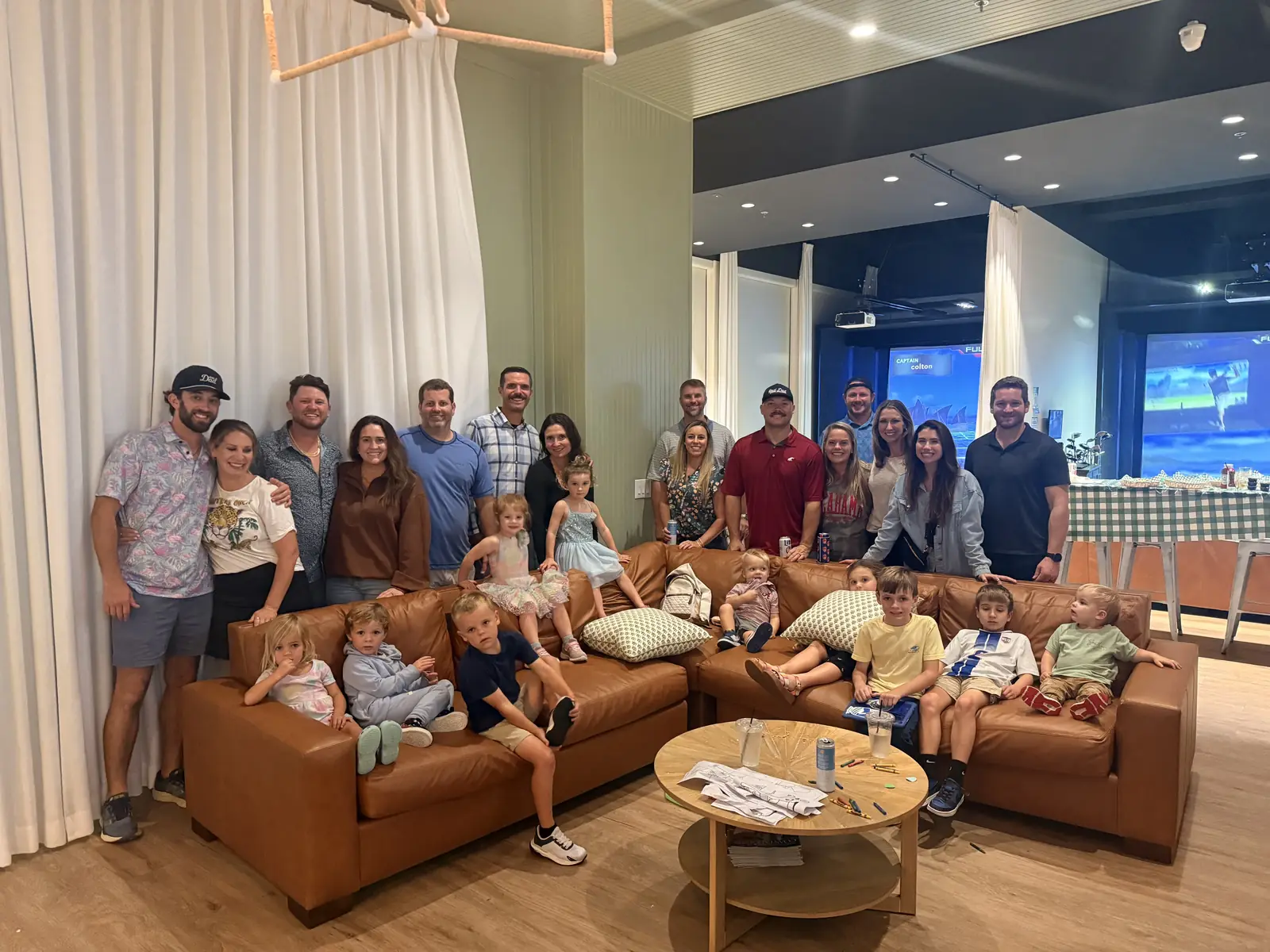 A large family group filling the lounge sofas at Tee Off at The Wharf, simulator screens lit behind them