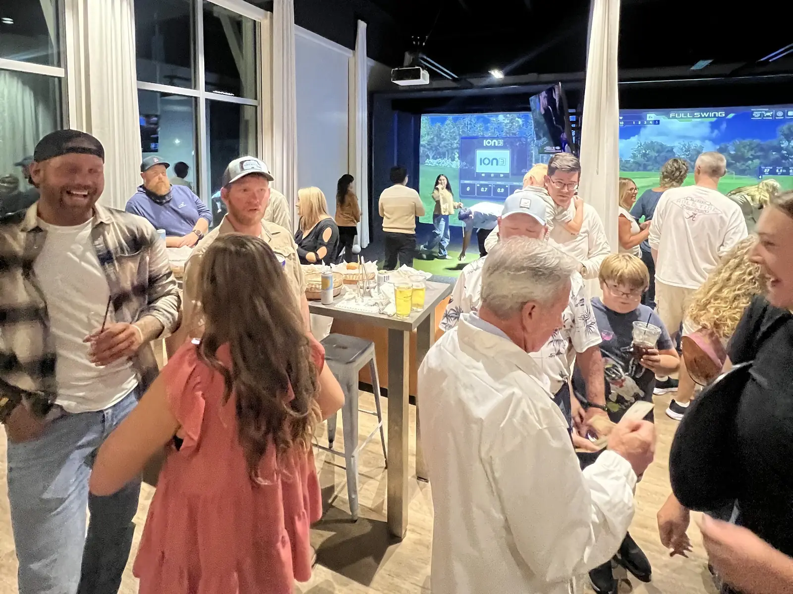 A busy night at Tee Off at The Wharf — guests and staff around the high tables with the bays lit behind