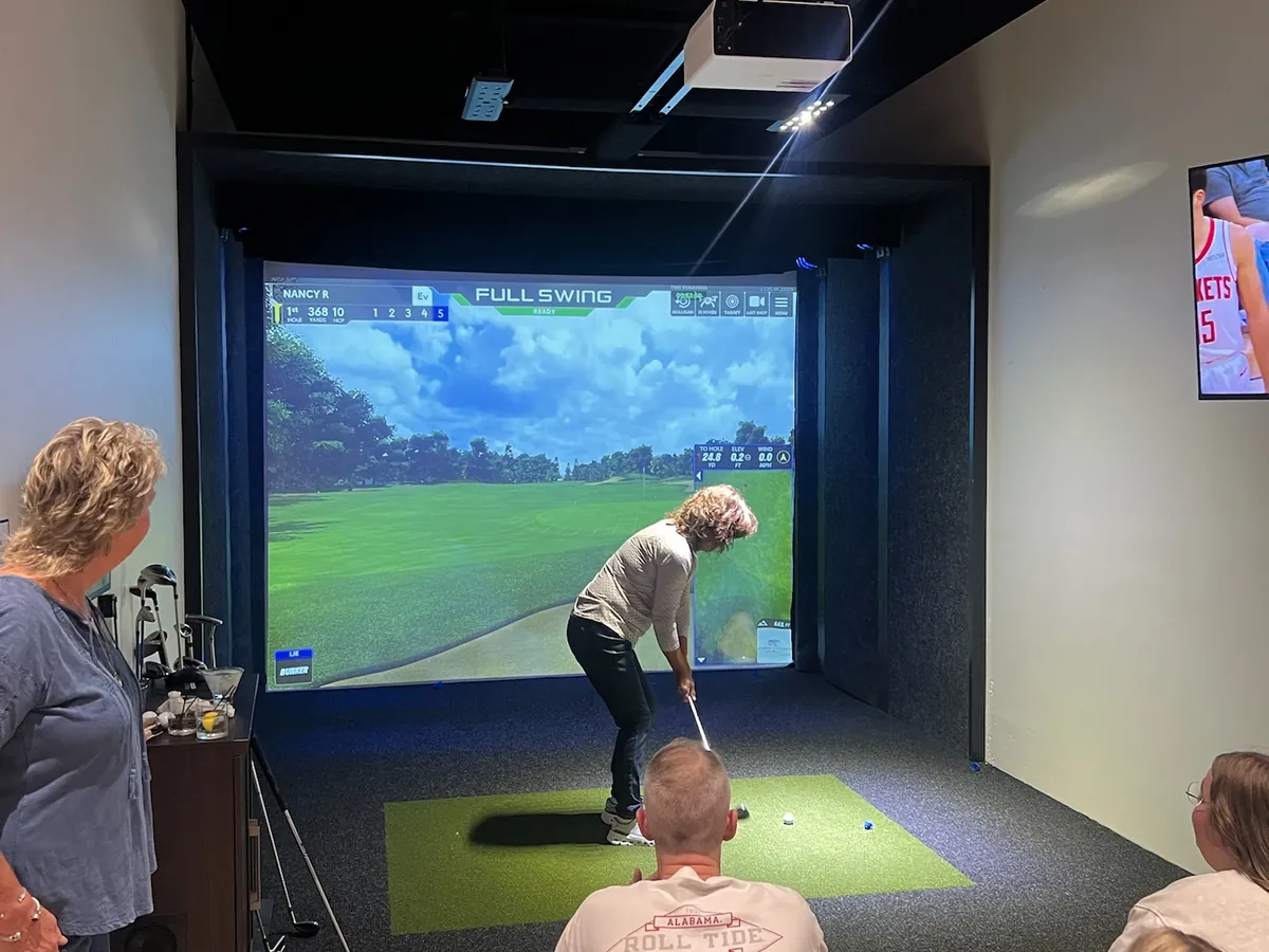 A golfer driving from the mat while friends watch from the bay at Tee Off at The Wharf