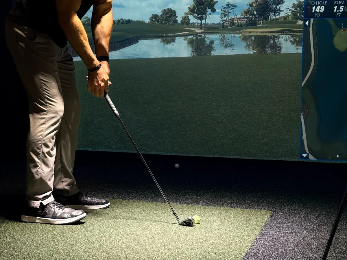 A golfer addressing the ball with a water carry on the screen at Tee Off at The Wharf